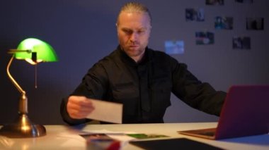 Kendine güvenen ciddi bir polis dizüstü bilgisayarla oturmuş fotoğrafları karşılaştırıyor. Polis departmanındaki suç davasını araştıran konsantre olmuş profesyonel polisin portresi..