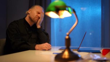 Karanlıkta lamba ışığıyla masada oturan yorgun polis gözlerini ovalıyor. Kafkasyalı erkek polis, kapalı alandaki suç davasını araştırmaktan yorulmuş. Aşırı çalışma kavramı.