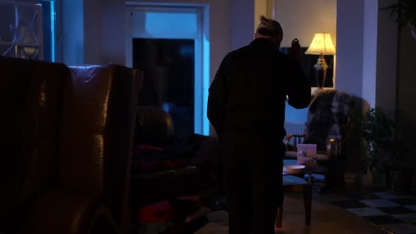 Back view policeman with flashlight walking inside robbed house collecting evidence. Wide shot Caucasian confident man in uniform examining crime scene in darkness indoors. — Stock Video