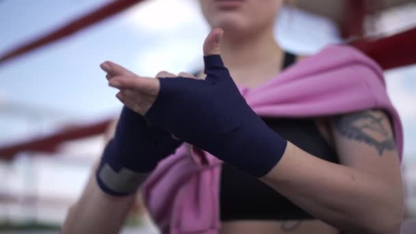 Detailní zábal boxovací obvaz na štíhlé ženské potetované ruce venku. Neznámá běloška se připravuje na cvičení na boxerském ringu na jaře letního dne. — Stock video