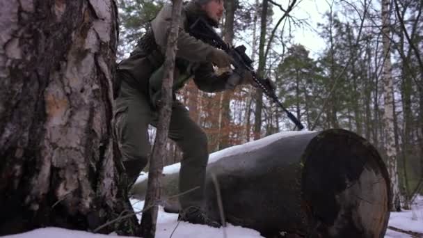 Panning menembak penembak jitu muda yang terkonsentrasi membidik dengan pistol di hutan musim dingin dalam gerakan lambat. Tentara Ukraina yang serius dengan senjata yang melihat keluar rumah. Konsep pertahanan dan konflik perang. — Stok Video