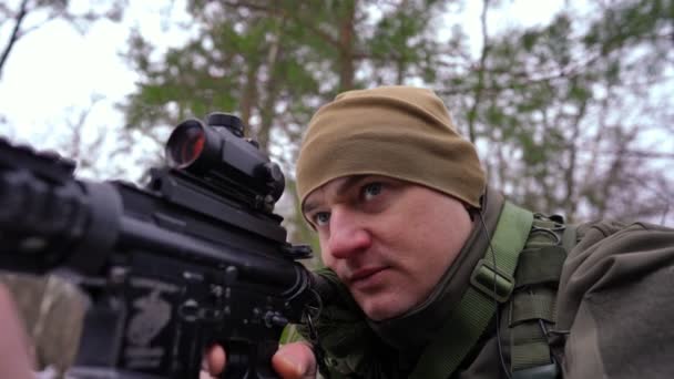 Großaufnahme konzentrierter vorsichtiger Soldat, der mit dem Gewehr wegschaut und in Zeitlupe über Kopfhörer spricht. Porträt eines ernsthaften tapferen ukrainischen Mannes im Wald im Freien. Aufklärung und Verteidigung. — Stockvideo
