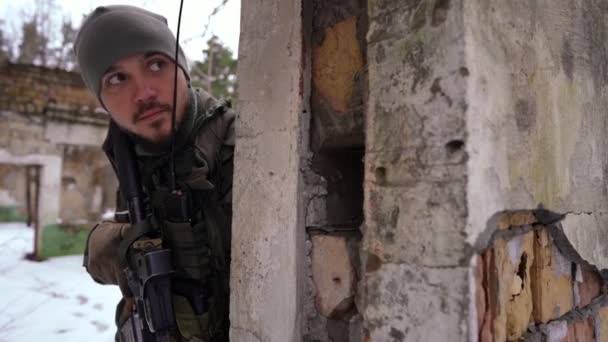 Elővigyázatos ukrán katona rejtőzik a lerombolt falnál, fegyverrel félrenéz. Egy jóképű, fiatal kaukázusi fegyveres férfi portréja hideg téli napon az orosz invázióról a romos városban.. — Stock videók