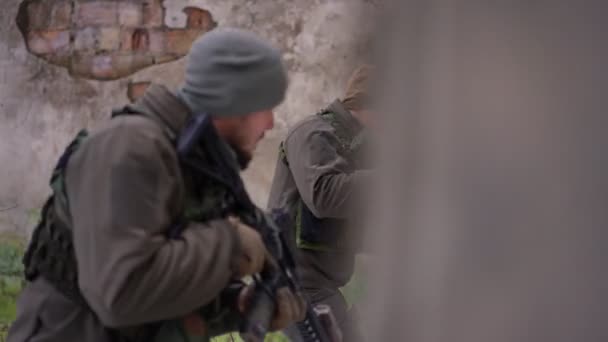 Side view two male soldiers gesturing passing ruined walls in city leaving with weapon. Courageous Ukrainian young men with guns walking in destroyed city in Ukraine in war zone. Military concept. — Stock Video