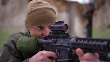 Ağır çekimde silahla ateş eden konsantre bir adamın portresi arka plandan gelen bulanık bir asker gibi. Ukrayna 'daki savaş bölgesinde odaklanmış Kafkas savaşçısı. Askeri işgal kavramı.
