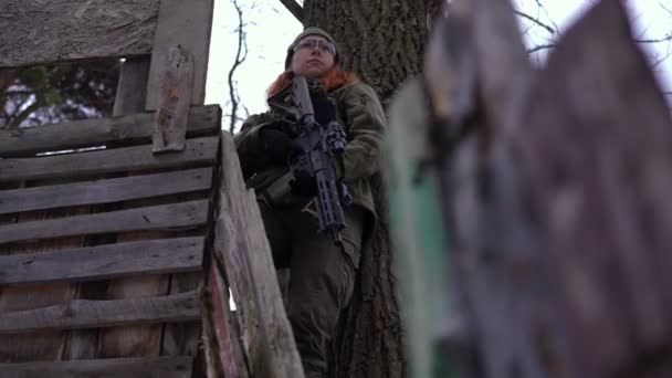 Gewapende mooie Oekraïense vrouw in uniform die naar de boom staat te kijken. Portret van zelfverzekerde blanke jonge soldaat buiten in oorlogsgebied. Moed en defensie concept. — Stockvideo