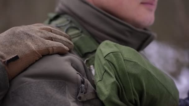 Acercamiento mano golpeando hombro de soldado irreconocible a cubierto al aire libre. Joven ucraniano defendiendo la independencia del país de pie con arma en bosque de invierno. — Vídeo de stock