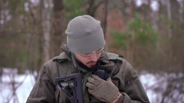 Vorderseite Porträt eines selbstbewussten jungen ukrainischen Mannes in Uniform, der im Walkie-Talkie spricht und lächelt. Tapferer kaukasischer Soldat steht im verschneiten Winterwald und erzählt Informationen des militärischen Geheimdienstes. — Stockvideo