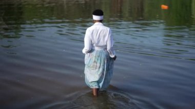 Arkadan bakan zayıf Afrikalı Afrikalı Amerikalı genç bir kadın nehire giriyor ve ağır çekimde ellerini uzatıyor. Geniş açılı, çıplak ayaklı kadın güneşli havanın tadını çıkarıyor. Yaşam tarzı ve eğlence..