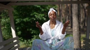 Ön manzara rahat Afro-Amerikan kadın nilüfer çiçekli açık havada meditasyon yaparken poz veriyor. Yavaş çekimde spordan zevk alan sakin, ince yogi portresi. Huzur ve güven.