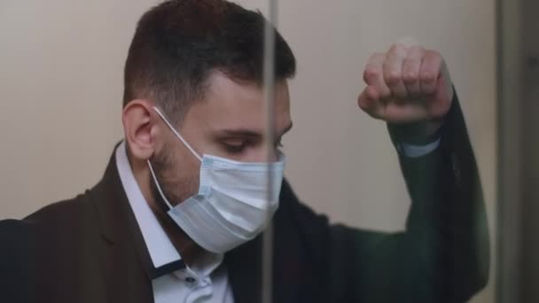 Närbild av frustrerad vit man i Covid-19 ansiktsmask stående i glas kontor och tänkande. Porträtt av stressad affärsman som har problem under coronavirus pandemi. — Stockvideo