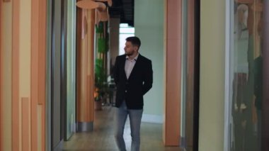 Genç yakışıklı, ciddi bir adam koridorda yürüyor ve düşünüyor. Kafkas işadamının iş yerinde gezinen portresi. Kendine güvenen başarılı erkek CEO etrafa bakıyor..