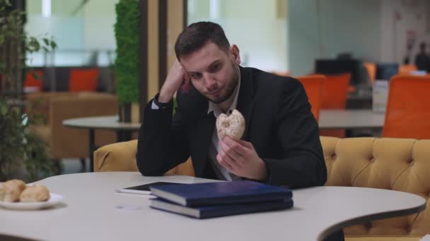 Молодой кавказский бизнесмен сидит за столом и ест пончики. Портрет стрессового красавца, врывающегося в дом. Концепция образа жизни и бизнеса. — стоковое видео