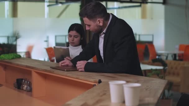 Portrait of concentrated young woman surfing Internet on tablet as focused man joining colleague at office bar and opening laptop. Portrait of successful business people working online. — Stock Video