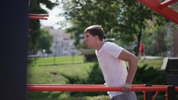 Portrait latéral de jeunes sportifs concentrés s'entraînant aux muscles des mains sur un plateau de gymnastique à l'extérieur. Ajustement concentré homme caucasien travaillant au ralenti dans le parc ensoleillé d'été de printemps. — Video