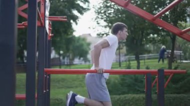 Parkın dışında jimnastik eğitimi alan aktif genç sporcu. Kafkasyalı formda sporcu yaz günü idman yapıyor. Sağlıklı yaşam tarzı ve dayanıklılık kavramı.