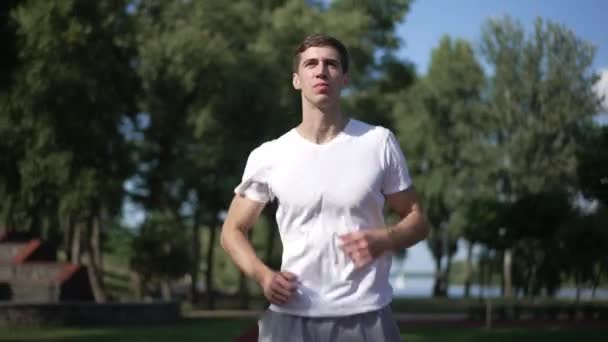 Widok z przodu pozytywny pewny siebie sportowiec biegający na świeżym powietrzu w parku pozostawiając. Biały młodzieniec biegający w słońcu. Zdrowy styl życia i koncepcja sportu. — Wideo stockowe