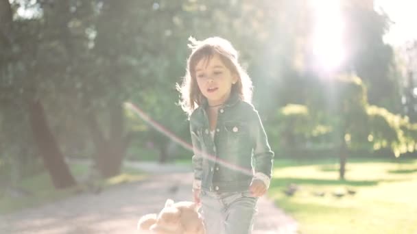 Carefree возбужденный европеец маленькая девочка прыгает с игрушкой в солнечный луч в парке вид спереди. Долли снимок счастливого расслабленного ребенка, получающего удовольствие от отдыха в весенний летний день. Медленное движение, камера. — стоковое видео