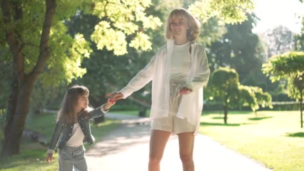 Relaksująca podekscytowana matka i córka stojące w słońcu, uśmiechnięte machające przed kamerą. biały piękne kobieta i słodkie dziewczyna pozowanie w sunbeam w zwolnionym tempie na zewnątrz. — Wideo stockowe