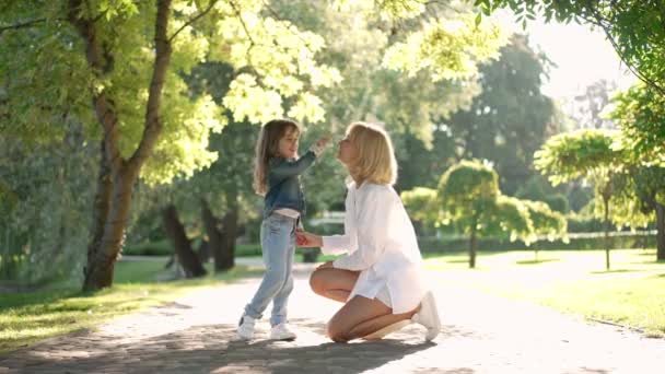 Geniş açılı mutlu beyaz anne ve kızı burnuna yavaşça dokunup gülümsüyor. Rahatlamış kadın ve kız hafta sonları güneşli yaz parkında eğleniyorlar.. — Stok video