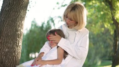 Mutlu genç anne kızını kucaklıyor saçlarını yavaş çekimde okşuyor ve konuşuyor. Güzel bir kızla yaz parkında eğlenen kendine güvenen beyaz bir kadının portresi..