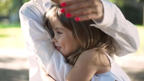 Encantadora menina caucasiana feliz abraçando mulher em câmera lenta sorrindo apontando para longe. Retrato da filha despreocupada excitada descansando com a mãe no parque de primavera de verão no dia ensolarado. — Vídeo de Stock