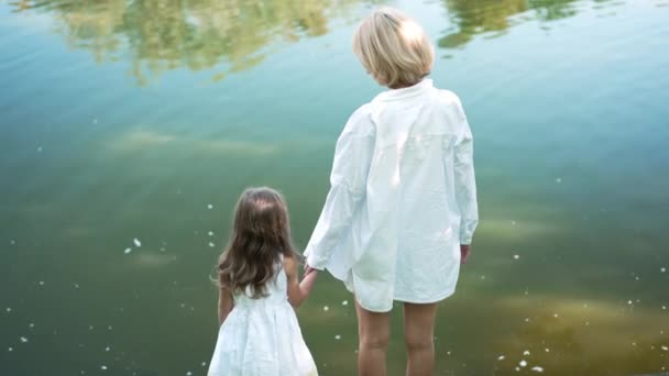 夏天的春天公园里，快乐的母亲和女儿手牵手站在湖水的后面。回头看快乐的白人女人和慢动作说话的女孩享受休闲. — 图库视频影像