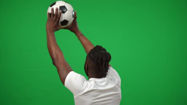 Back view tattooed African American man raising ball in hands rejoicing goal at chromakey background template. Happy excited sportsman gesturing looking away on green screen. Success and sport concept — стоковое видео