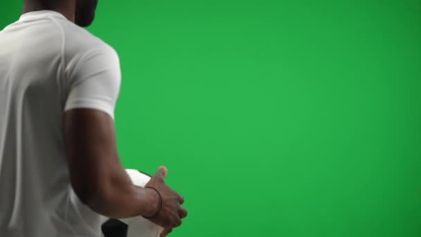 バックビュー若いアフリカ系アメリカ人選手が左手でボールを渡すから緑の画面を歩いて表示されます。クロマキーのバックグラウンドでゲームをプレイするスポーツマンを確信しています。サッカー選手権のコンセプト. — ストック動画