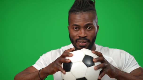 Motivated confident African American sportsman squeezing football ball looking at camera. Front view portrait of concentrated man posing at green screen chromakey background. — стоковое видео