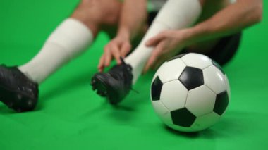 Yeşil ekranda, arka planda tanınmayan bir sporcunun yaralı ayak bileğini tuttuğu yakın plan futbol topu. Kromakey arka planda ağrılı bacağı olan genç beyaz bir adam..