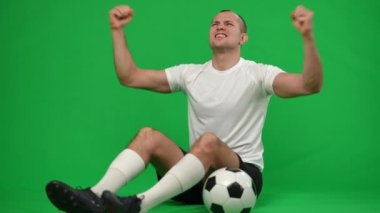 Kromakey arka planında futbol topuyla oturan heyecanlı Kafkas sporcusu. Mutlu gülümseyen genç futbolcunun portresi yeşil ekranda neşe dolu bir başarı..