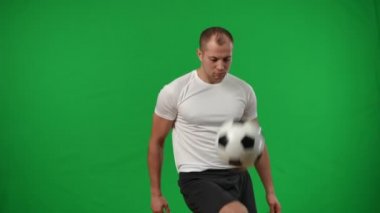 Genç sporcu, krom arka planda bacağıyla futbol topunu yakalıyor ve kameraya bakıyor. Beyaz perdede ağır çekimde poz veren ciddi bir beyaz futbolcunun portresi.