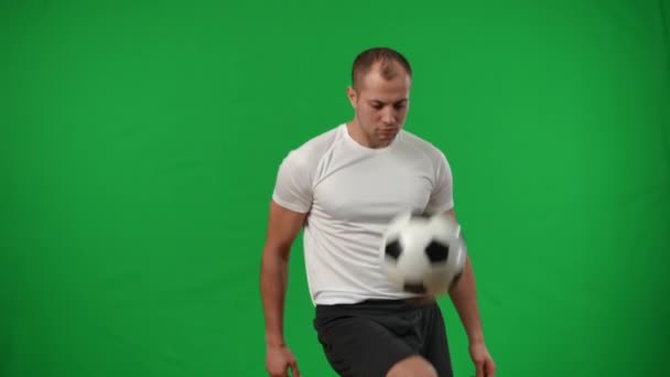 Jovem desportista focado pegando bola de futebol com a perna em fundo cromado e olhando para a câmera. Retrato de jogador profissional sério caucasiano posando em câmera lenta na tela verde. — Vídeo de Stock