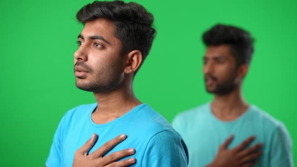 Side angle view two concentrated proud Middle Eastern men singing national anthem with hand on chest. Handsome young football fans at chromakey green screen background looking away. — стоковое видео