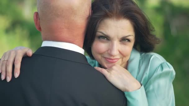Porträt einer zufriedenen selbstbewussten Frau, die in die Kamera lächelt und einen Mann im Anzug umarmt, der draußen im Park steht. Glücklich schöne kaukasische Frau posiert in Zeitlupe mit elegantem Ehemann. — Stockvideo