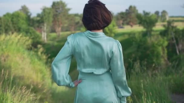 Back view confident slim woman standing outdoors admiring beauty of nature on summer spring day. Relaxed Caucasian elegant lady enjoying leisure in park outdoors on sunny day. Slow motion. — ストック動画