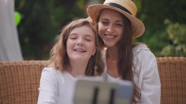 Vooraanzicht zorgeloos vrolijke jonge vrouw en tienermeisje gezichten maken selfie op smartphone buiten. Fijne ontspannen blanke zussen die plezier hebben in de achtertuin in het weekend. Langzame beweging. — Stockvideo