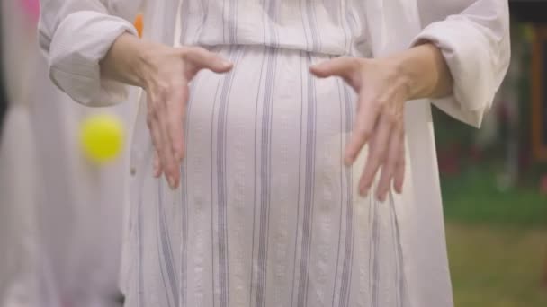 Збільшені жіночі руки жестикулюють серцеву форму на вагітному животі в повільному русі. Нерозпізнане кавказьке чекання стоїть на подвір'ї. Материнство і вагітність. — стокове відео