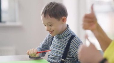 Heyecanlı otistik çocuk portresi bulanık, tanınmayan bir kadın olarak gülümsüyor. Akli dengesi bozuk mutlu beyaz çocuk evde annesiyle resim yapmaktan zevk alıyor..