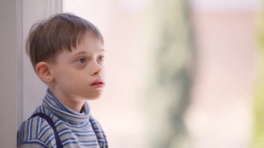 Kafkasyalı otistik çocuk pencerenin önünde durmuş başka tarafa bakıyor. Güneşli bir günde evde zihinsel bozukluğu olan bir çocuğun portresi. Yaşam tarzı ve otizm kavramı.