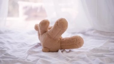 Kapalı alanda yatmakta olan yakın plan kahverengi ayıcık. Güneşli bir günde beyaz çarşafta yatak odasında oyuncak. Çocukluk kavramı.