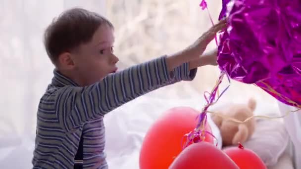 Gefascineerde autistische blanke jongen die thuis met leeggelopen ballonnen speelt. Side view portret van curios gelukkig ontspannen kind met geboorte anomalie genieten van vrije tijd met speelgoed. Autisme en nieuwsgierigheid. — Stockvideo