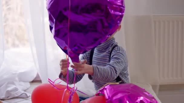 Παιγνιώδη αυτιστικό αγόρι σκάει μπαλόνι κάθεται στο σπίτι μέσα. Πορτρέτο του Curios συμπυκνωμένο Καυκάσιο παιδί με ψυχική διαταραχή παίζοντας απόλαυση αναψυχής. Έννοια της ασθένειας και του τρόπου ζωής. — Αρχείο Βίντεο
