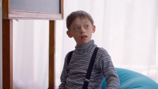 Curios αυτιστικό αγόρι κάθεται στην καρέκλα τσάντα στην τάξη ακούγοντας δείχνοντας μαυροπίνακα. Πορτρέτο Καυκάσιου παιδιού με ανωμαλία γέννησης που σπουδάζει στο σχολείο. Εκπαίδευση και αυτισμός. — Αρχείο Βίντεο