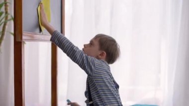 Sınıfın içinde kumaşla karatahtayı temizleyen neşeli otistik öğrenci portresi. Doğum anomalisi olan mutlu, gülümseyen beyaz çocuk okulda okuyor. Otizm ve zeka.