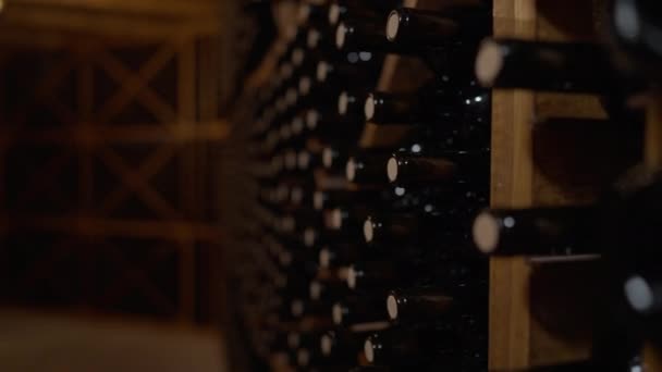 Kamera na żywo porusza się wzdłuż rzędów korkowych butelek wina ułożonych w piwnicy w pomieszczeniach. Drogi napój wysokiej jakości w winiarni w ciemności. Koncepcja luksusowa i winiarska. — Wideo stockowe