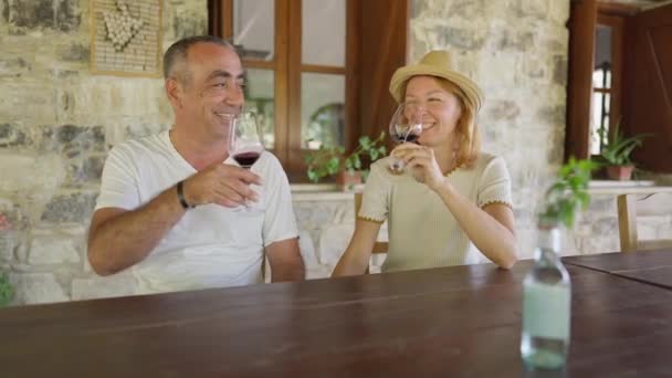 Mutlu, beyaz bir çift dışarıda oturmuş şarap tadıyor ve gülümsüyor. Kıbrıs Rum Kesimi 'nin terasındaki restoranda yaz tatilinin keyfini çıkaran olumlu bir erkek ve kadın. Yavaş çekim. — Stok video