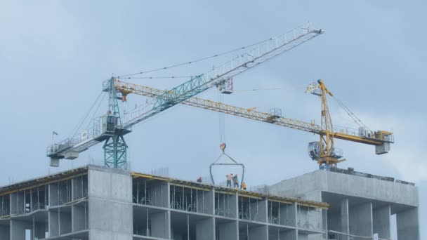 Grues à tour larges sur le chantier avec des travailleurs masculins caucasiens déchargeant des matériaux de construction. Des hommes qui travaillent au-dessus d'un bâtiment en construction à l'extérieur. Construction de gratte-ciel en Kiev — Video