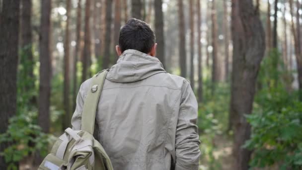 Tracking shot van zelfverzekerde mannelijke avonturier met rugzak lopen in slow motion in het bos draaien gebaren uitnodigen om mee te reizen. Achteraanzicht portret van blanke man wandelen buiten poseren. — Stockvideo